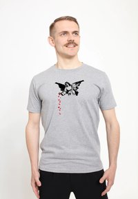 Šedé bavlněné tričko s černou grafikou anděla a červenými akcenty ve tvaru srdce, které kaskádovitě splývají dolů. Krátké rukávy a kulatý výstřih.