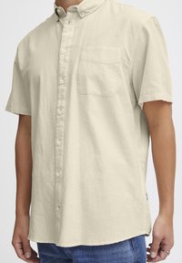 Korte mouw knoopshirt in lichtbeige stof. Bevat een button-down kraag, een borstzak en een relaxte pasvorm.