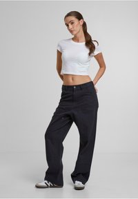 Pantalones anchos negros de cintura alta, con bolsillos frontales y sutiles detalles dorados, combinados con un top corto blanco ajustado y zapatillas.