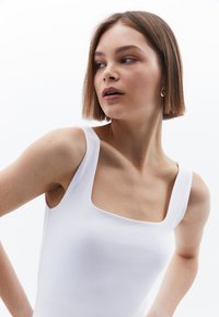 Witte, aansluitende tanktop met een vierkante halslijn en brede bandjes. Soepele stoftextuur, minimalistisch design zonder zichtbare patronen of accenten.