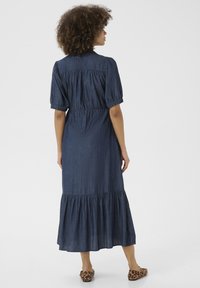 Jeansmaxiklänning med puffärmen, samlat midja och flikig nederkant. Mörkblå färg. Modellen bär djurmönstrade slip-on skor.
