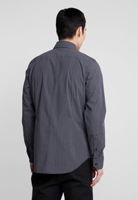 Černo-bílá košile se vzorem cik-cak, s špičatým límečkem, dlouhými rukávy a knoflíkovými manžetami. Tkanina se zdá být lehká s hladkou texturou.