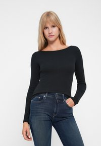 Top negro de manga larga con escote barco, diseño ajustado y textura ribeteada, combinado con jeans de mezclilla azul oscuro.