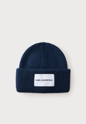 Bonnet en maille côtelée bleu marine avec un revers plié et une étiquette rectangulaire blanche indiquant "KARL LAGERFELD" en lettres noires.