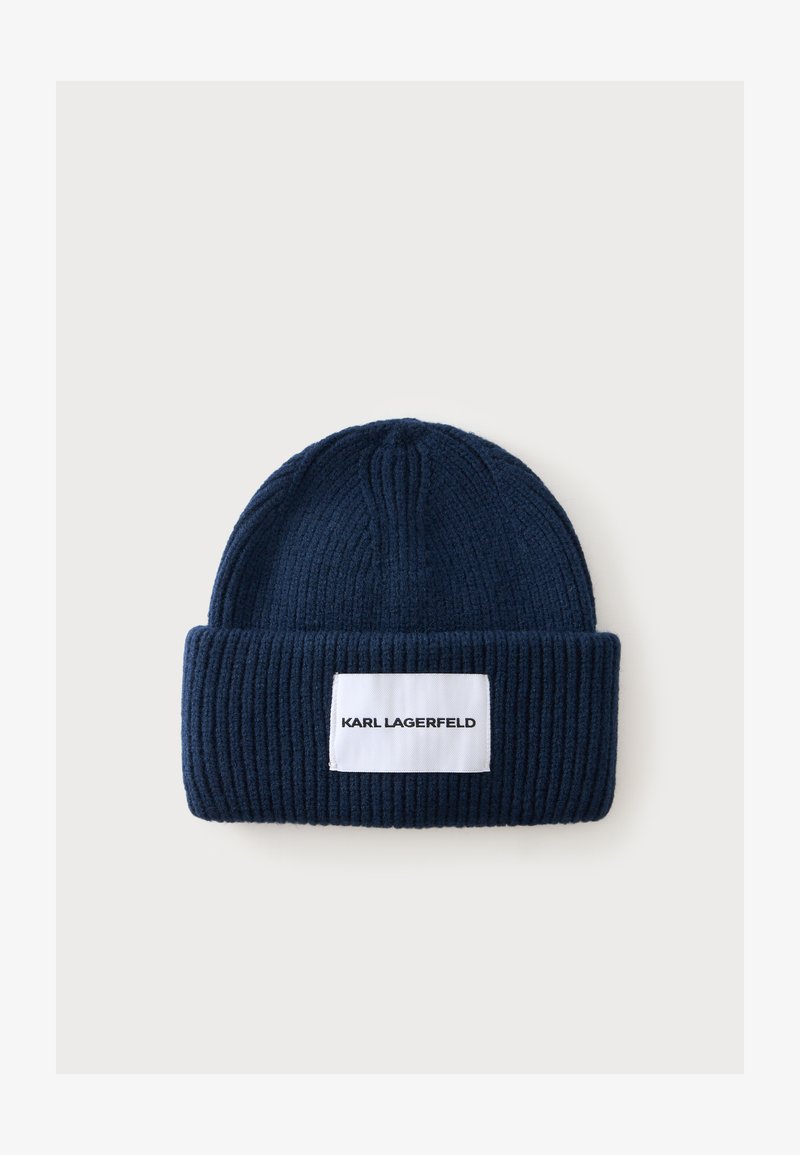 Bonnet en maille côtelée bleu marine avec un revers plié et une étiquette rectangulaire blanche indiquant "KARL LAGERFELD" en lettres noires.