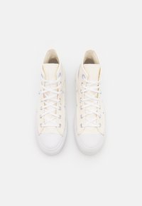 Bílé vysoké tenisky z plátna v krémové barvě s bílými gumovými podrážkami. Vyznačují se vícebarevnými vyšívanými akcenty hvězd a měsíce. Bílé tkaničky.