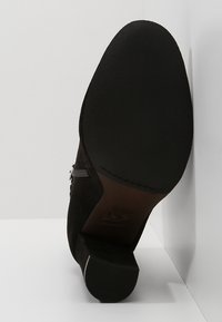 Zapato de tacón de ante negro con suela de goma texturizada, cierre lateral con cremallera y tacón de altura media ligeramente afilado.
