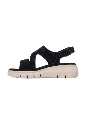 Sandalia negra con diseño recortado y correa ajustable. Cuenta con una parte superior texturizada y una suela beige ligera con detalles acolchados.