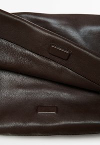 Dark brown leather material folded with visible rectangular buttonholes or stitched details on a smooth, slightly textured surface.