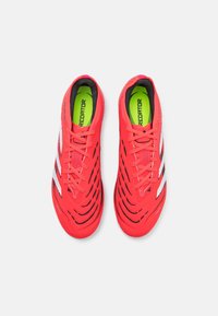 Zapatillas deportivas rojas con un diseño texturizado, que presentan franjas blancas, acentos negros y una plantilla de color verde brillante. También son visibles los cordones cortos.