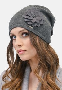 Šedý pletený beanie klobouk s plstěnou květinovou ozdobou se středem zdobeným rhinestonem. Měkká textura a uvolněný design vhodný pro každodenní nošení.