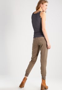 Grå ribbet tanktop med bølget halslinje, kombinert med beige smale bukser og brune hælankelboots. Glatt tekstur og tettsittende design.