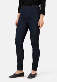 Jeans ajustados de mezclilla oscura con una cintura alta, con detalles de costura naranja y una textura suave. Combinados con zapatos planos negros.