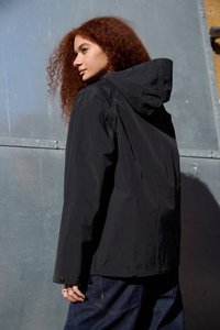 Sort vandtæt jakke med hætte, der har en afslappet pasform, synlige sømme og tryklåse på ærmerne. Stylet med denim bukser.