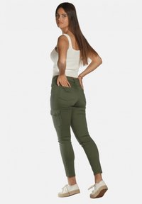 Pantalons cargo verts olives en coton mélangé, coupe slim avec poches latérales, associés à un débardeur blanc à côtes et des espadrilles claires.