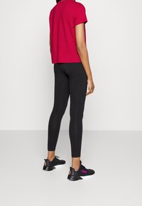 Magenta short-sleeve top paired with black leggings and black sneakers featuring pink accents and a textured design. View from behind.