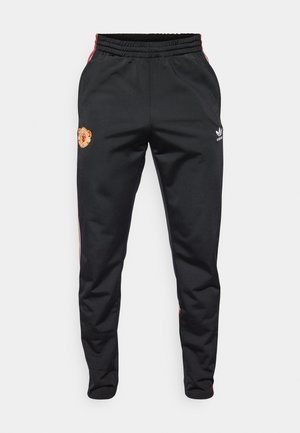 Black athletic pants with an elastic waistband, featuring red side stripes, a Manchester United logo, and an Adidas emblem in white.