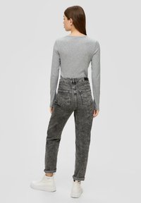 Graues Langarmoberteil kombiniert mit hoch taillierten, ausgewaschenen schwarzen Jeans. Strukturiertes Material, umgeschlagene Säume und weiße Sneaker runden den Look ab.