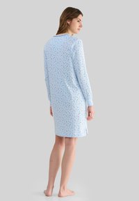 Camisón azul claro de manga larga, con un pequeño patrón floral, fabricado en tejido suave y con aberturas laterales para mayor comodidad en el movimiento.
