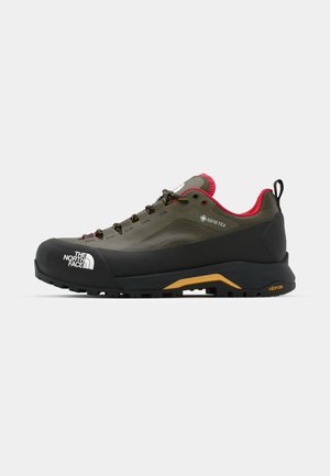 GORE-TEX hiking shoe in olive green with black rubber toe cap and midsole. Features black and yellow Vibram outsole, pink accents, and laces.
