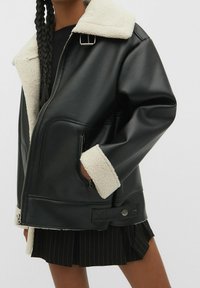 Chaqueta de cuero sint�ético negra con un collar y puños de forro polar crema, con cierre de cremallera en la parte delantera, bolsillos laterales y un detalle de cierre a presión.