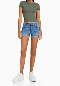 Grön tajt t-shirt, blå denimshorts med framfickor och rullad fåll, tillsammans med vita plattformssneakers. Avslappnad sommaroutfit.