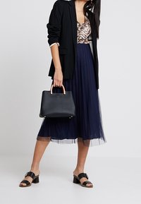 Blazer nero, top floreale, gonna midi in tulle blu navy, sandali neri e una borsa nera strutturata con manico in tonalità oro.