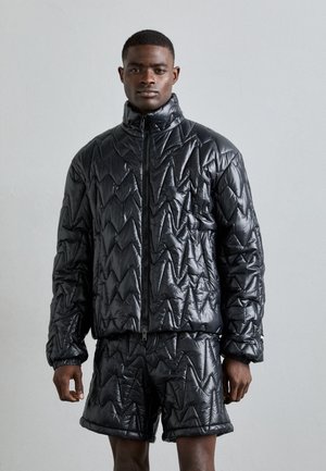 Quilted black puffer jacket with a high collar and zip closure, featuring a zigzag pattern, paired with matching shorts. Smooth, shiny texture.