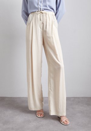 Pantaloni beige a gamba larga realizzati in tessuto leggero, con vita elastica e cordoncino regolabile, e tasche laterali. Texture morbida.