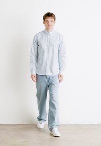Chemise boutonnée à rayures bleu clair associée à un jean bleu clair et des baskets blanches. La chemise a un col classique et des manches longues.