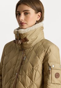 Karma ar kvadrātveida šuvēm, augstu apkakli, vilnas oderi, brūniem akcentiem un vairākiem rāvējslēdzējiem. Uz piedurknes ir uzšūta emblēma.