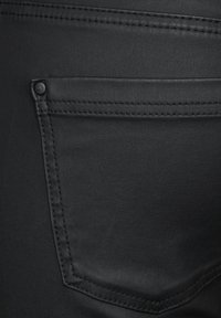 Jeans negros con un bolsillo trasero con un botón en tono, costuras visibles y un acabado de tela suave y ligeramente texturizado.