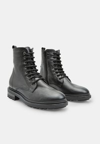 Stivali alla caviglia in pelle nera con finitura testurizzata, lacci frontali e zip laterale. Sole in gomma spessa con motivo a scanalature per una migliore aderenza.