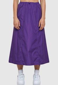 Lilla midikjole laget av lett materiale, med elastisk midjebånd med snor og to glidelåslommer på sidene.