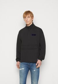 Felpa nera con zip, colletto alto, polsini elasticizzati, tasca frontale e logo ricamato blu. Realizzata in un tessuto testurizzato.