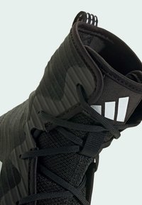 Musta urheilukenkä, jossa on teksturoitu synteettinen päällinen, verkkopaneelit, nauhakiinnitys ja kolme valkoista raitaa korostamassa nilkkaa.