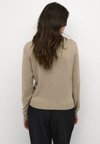 Kremveidīgs adīts džemperis ar apaļu kakla izgriezumu un ribotām aprocēm. Ievērojama brīva piegriezuma un gluda struktūra, apvienota ar melnām biksēm.