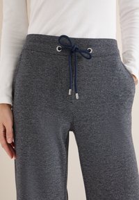 Granatowe dresy wykonane z miękkiej, teksturowanej tkaniny. Posiadają ściągacz w pasie ze srebrnymi zakończeniami sznurka oraz boczne kieszenie.