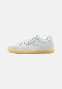 Sneaker bianche in pelle con una texture liscia, dettagli a perforazione, e suola in gomma naturale. Presentano lacci bianchi e etichetta del marchio sul lato.