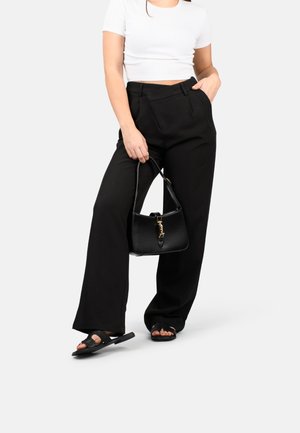 Zwarte wijde broek met een op maat gemaakte pasvorm en voorzakken, gecombineerd met een zwarte handtas met gouden accenten. Het model draagt zwarte sandalen.