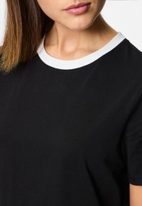 Must mustaga t-särk valge ümmarguse kaelusega, millel on pehme kangatekstuur ja lühikesed varrukad. Kaeluse ääres on nähtav õmblus.