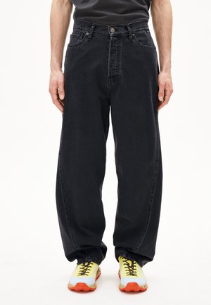 Jeans in denim nero con una vestibilità ampia, caratterizzati da un'alta vita, cinque tasche e una chiusura con bottone. Abbinati a scarpe da ginnastica multicolori.