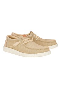 Zapatos de lona beige con cordones beige, que cuentan con una suela de goma texturizada con motas y un diseño cosido en los bordes. Acento de cuero en el talón.