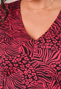 Tessuto a motivo rosa e nero caratterizzato da una combinazione di strisce zebrate e macchie, con un design a profondo scollo a V e una consistenza morbida.