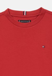 Rød bomull T-skjorte med rund hals, med en liten brodert logo i blått, hvitt og rødt på venstre bryst. Myk tekstur.