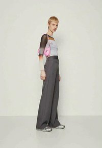 Pantalones de pierna ancha grises combinados con una blusa de manga larga de degradado y un pequeño bolso rosa. Zapatillas plateadas completan el conjunto.