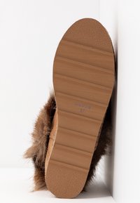 Sula på en brun, pälsfodrad sko som visar mönster och storlek 37 med "Tillverkad i Spanien" text på en vit bakgrund.