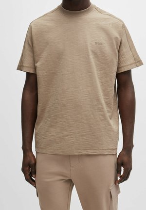 Beige T-Shirt mit kurzen Ärmeln und Rundhalsausschnitt, fein strukturiert. Mit Logo auf der Brust, legerer Passform und geradem Saum.