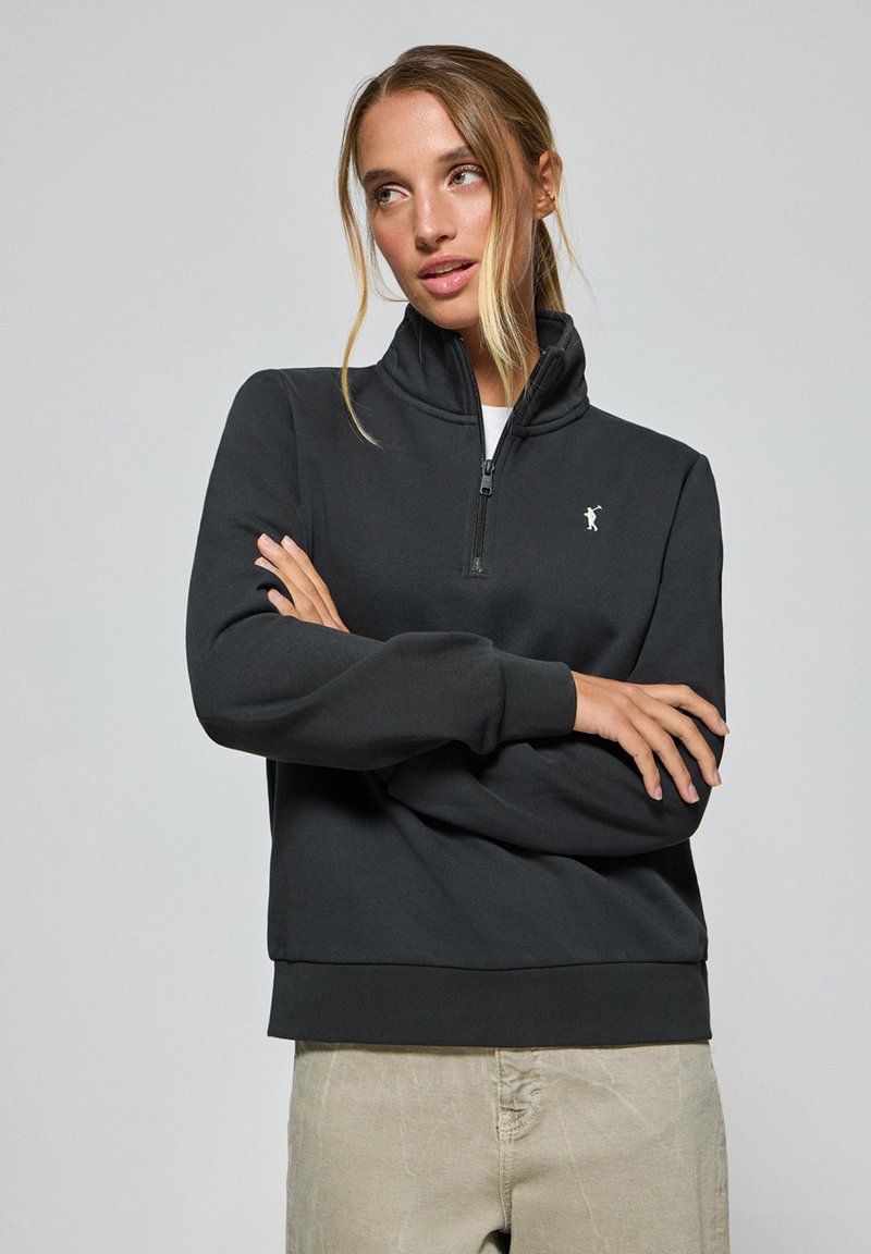 Svart sweatshirt med hög krage, halv dragkedja och vitt logotyp, med långa ärmar och ribbade muddarn, tillverkad av mjukt, strukturerat tyg.