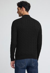 Czarny sweter w splot kabelkowy z wysokim kołnierzem, prążkowanymi mankietami i dołem, prezentujący teksturowany wzór i dopasowaną sylwetkę.
